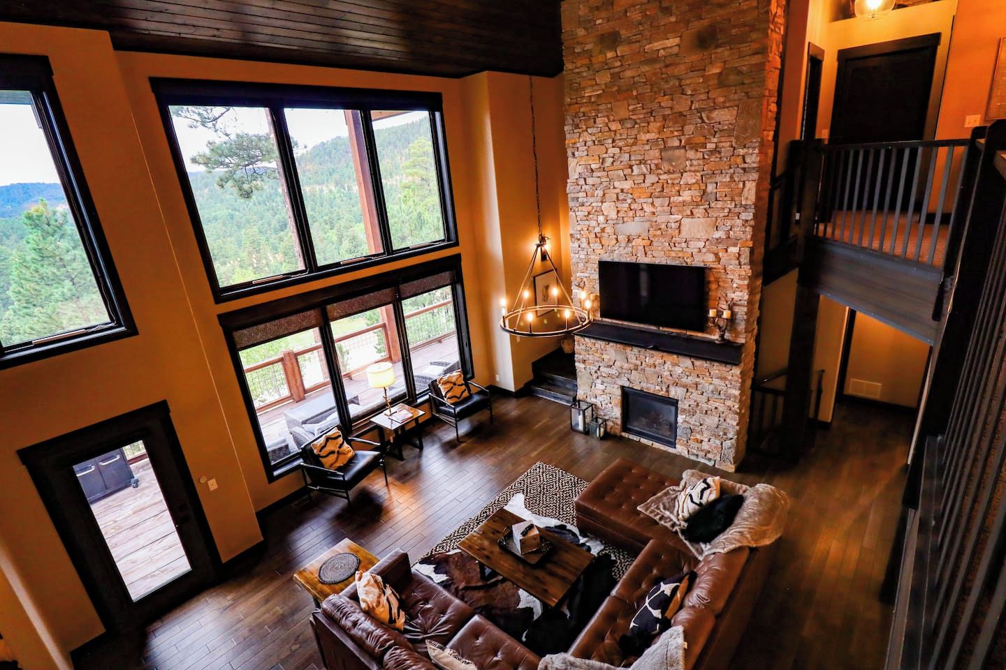A spacious living room with a stone fireplace, large windows, and a high ceiling.