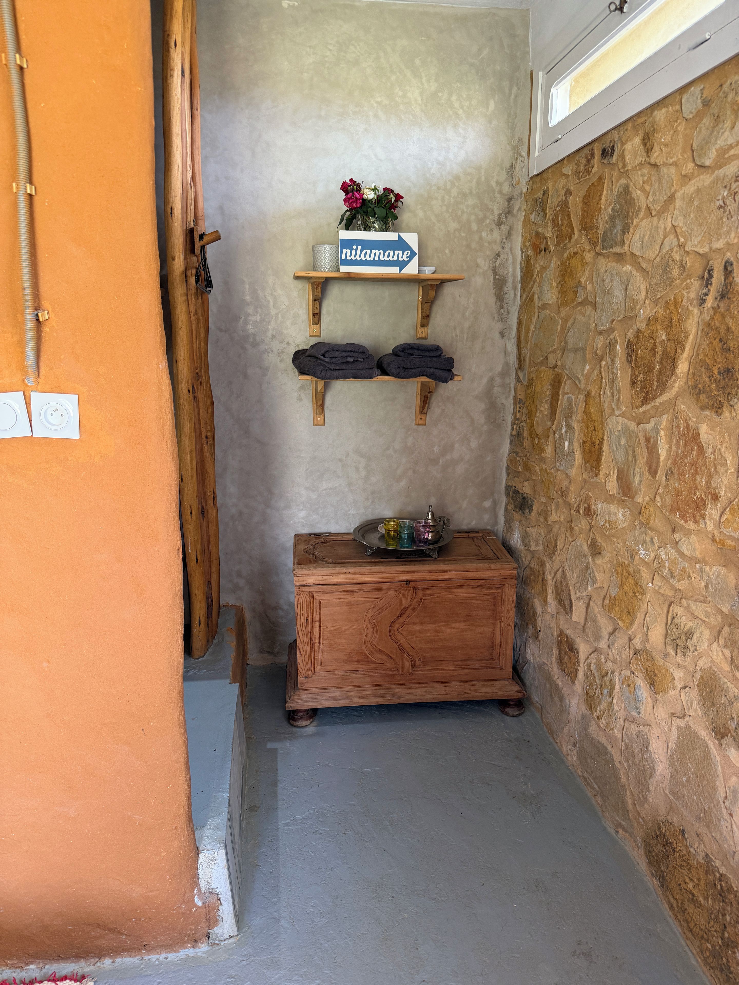 A narrow hallway with a wooden bench, a stone wall, and a small shelf with a sign.