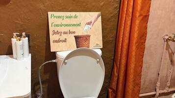 A bathroom with a toilet, a hand sanitizer dispenser, and a sign encouraging environmental care.