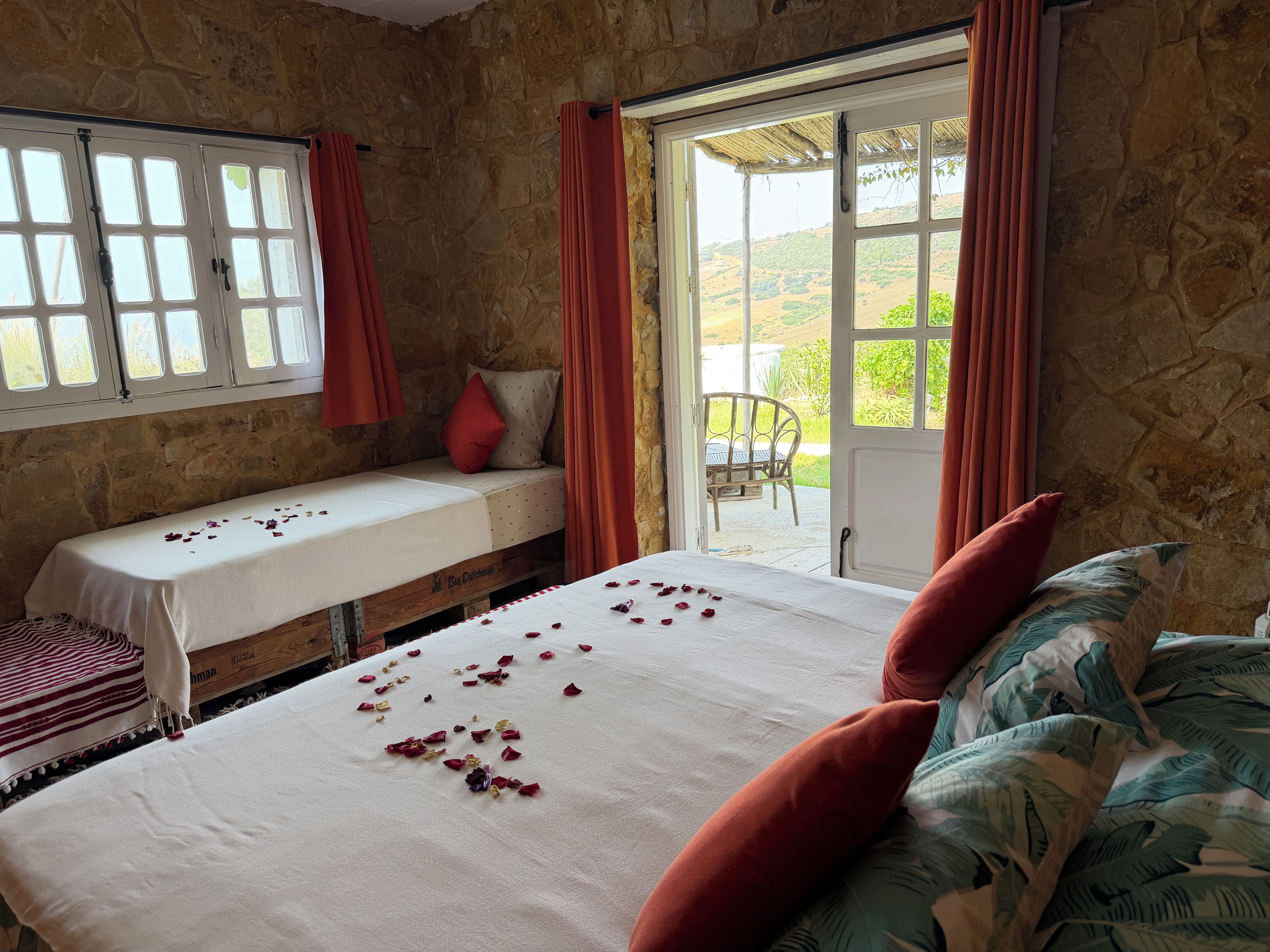 Una habitación con cama, un banco y vista a la vegetación exterior.