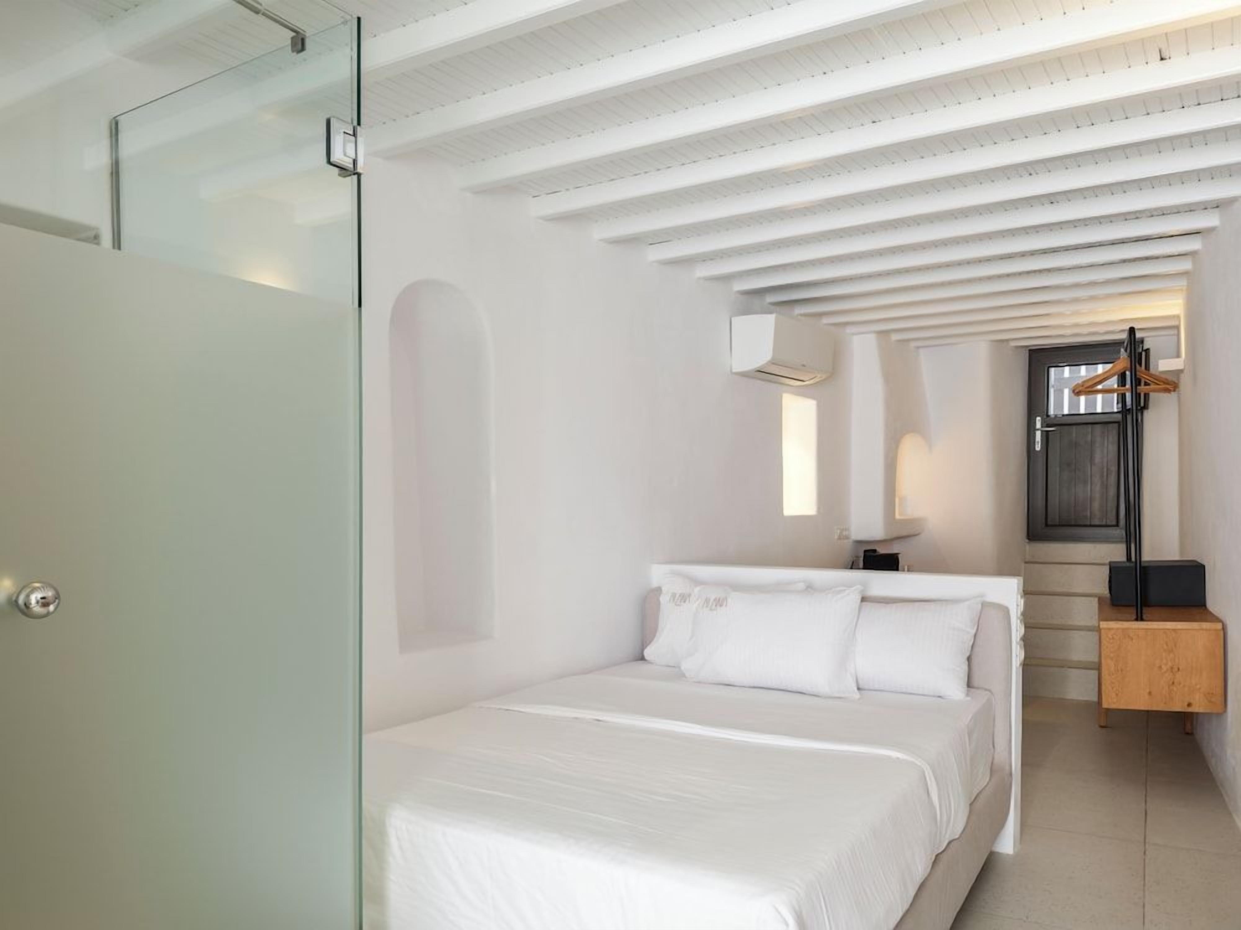 A modern bedroom with a bed, a wooden nightstand, a hanging light, and a door with a frosted glass panel.