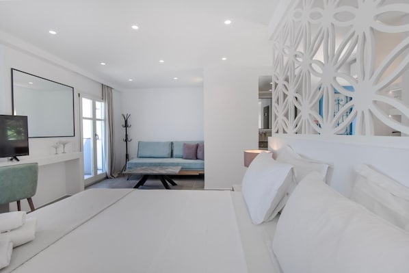 A modern bedroom with a large bed, a TV, and a decorative wall panel. - Alexandros Studios and Apartments (Paros)