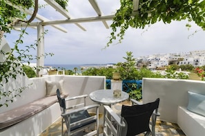 A terrace with a white outdoor seating area, a round table, and a view of a coastal town. - Alexandros Studios and Apartments (Paros)