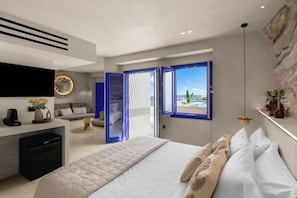 A modern hotel room with a large bed, a seating area with a sofa, a desk with a coffee machine, and a view of the sea through a large window. - Alexandros Studios and Apartments (Paros)