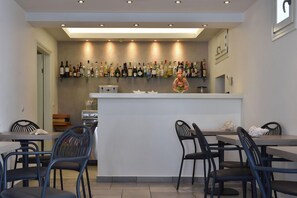 A bar area with a countertop and shelves of bottles, two tables with chairs, and a door leading to another room. - Alexandros Studios and Apartments (Paros)