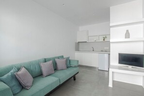 A modern living room with a teal sofa, a flat-screen TV, and a minimalist kitchen in the background. - Alexandros Studios and Apartments (Paros)