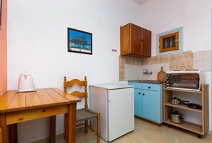 A compact kitchen with a wooden table, a small refrigerator, a blue cabinet, and a vintage toaster. - Alexandros Studios and Apartments (Paros)