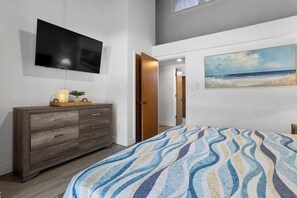 A bedroom with a bed, a TV mounted on the wall, a wooden dresser, and a painting of a beach scene. - 657 Olde Camelot Circle (Haines City)