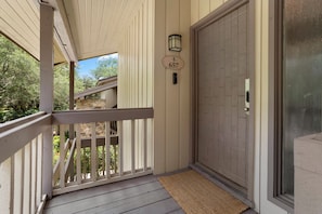 A covered porch with a wooden railing, a door with a number plate, and a small outdoor area with a view of greenery. - 657 Olde Camelot Circle (Haines City)