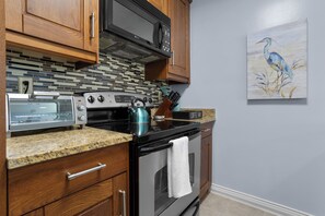 A kitchen with wooden cabinets, a microwave, a stove, and a coffee bar sign. - 657 Olde Camelot Circle (Haines City)