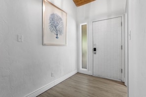 A hallway with a white textured wall, a framed artwork, a white door with a frosted glass panel, and a wooden floor. - 657 Olde Camelot Circle (Haines City)