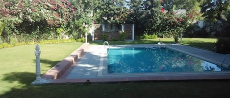 Une piscine rectangulaire dotée d’une terrasse dallée, entourée d’une pelouse bien entretenue et d’arbustes en fleurs.