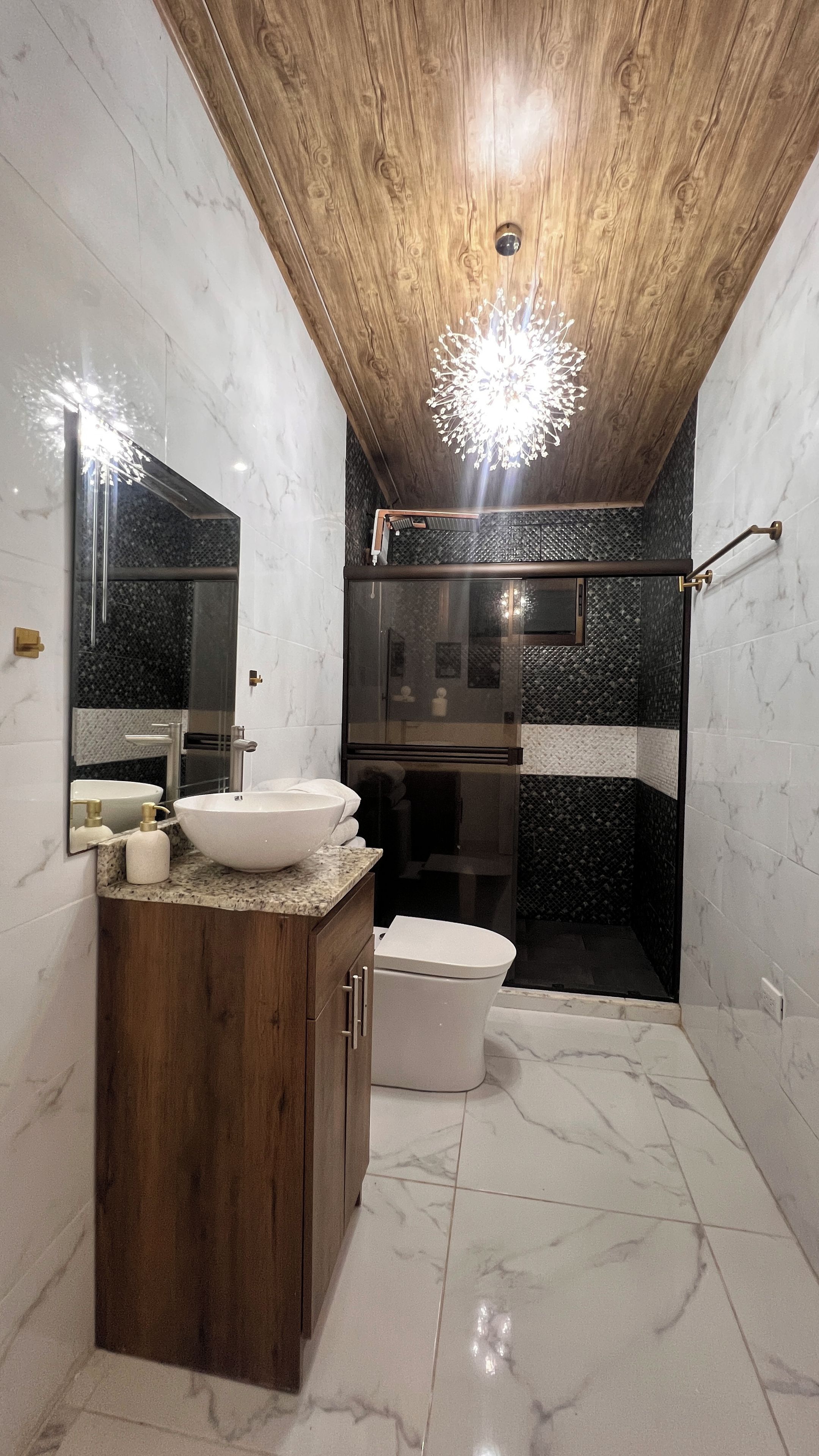 Une salle de bain moderne avec un plafond en bois, un lavabo sur pied, une douche à parois de verre et un revêtement de sol en marbre.