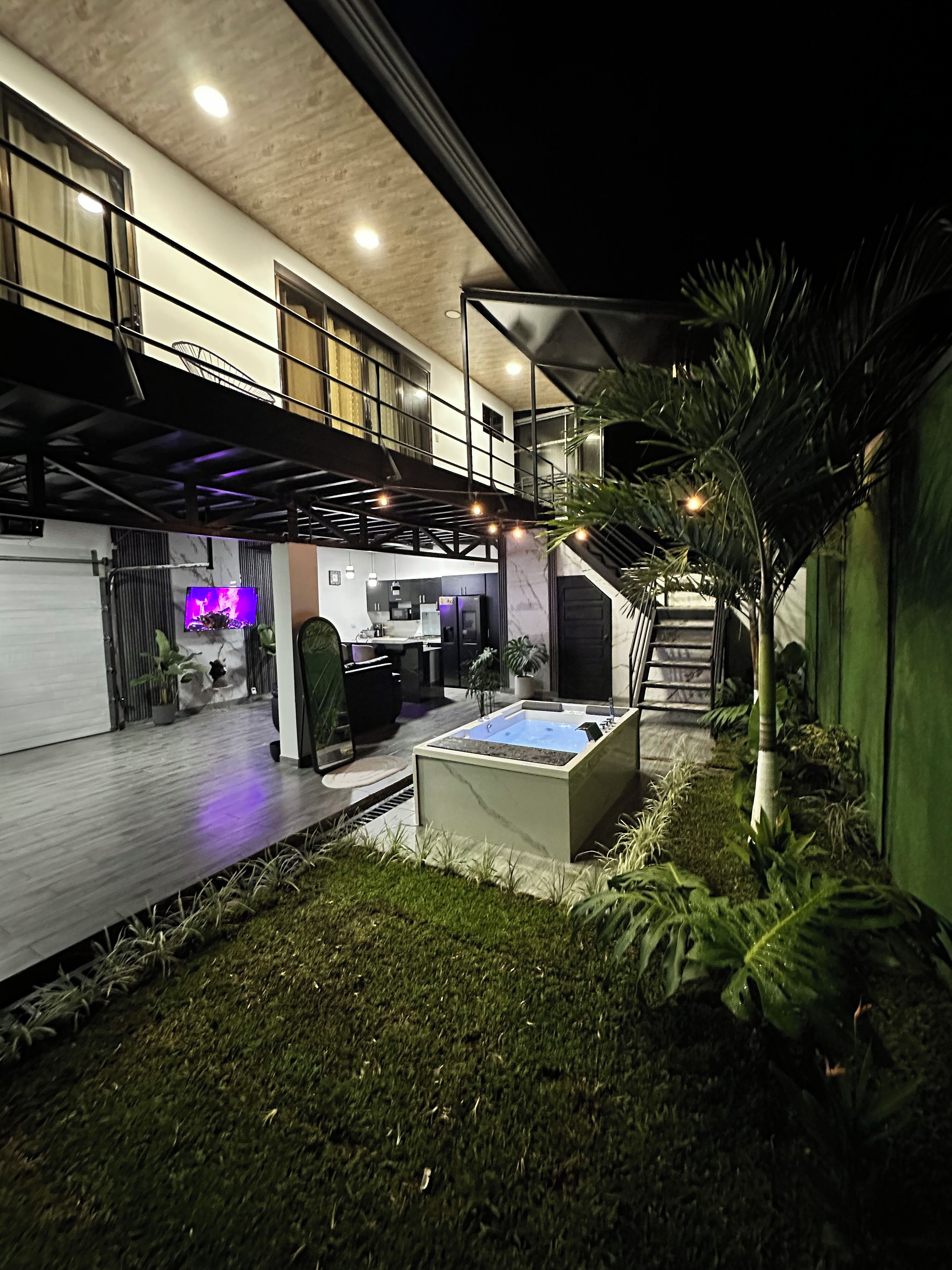 A modern outdoor space with a hot tub, a staircase, and a kitchen area.