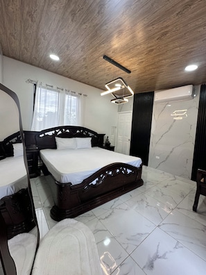 Une chambre avec un plafond en bois, un lit avec une tête de lit, une table de chevet, un miroir, une fenêtre avec des rideaux et un appareil de climatisation.