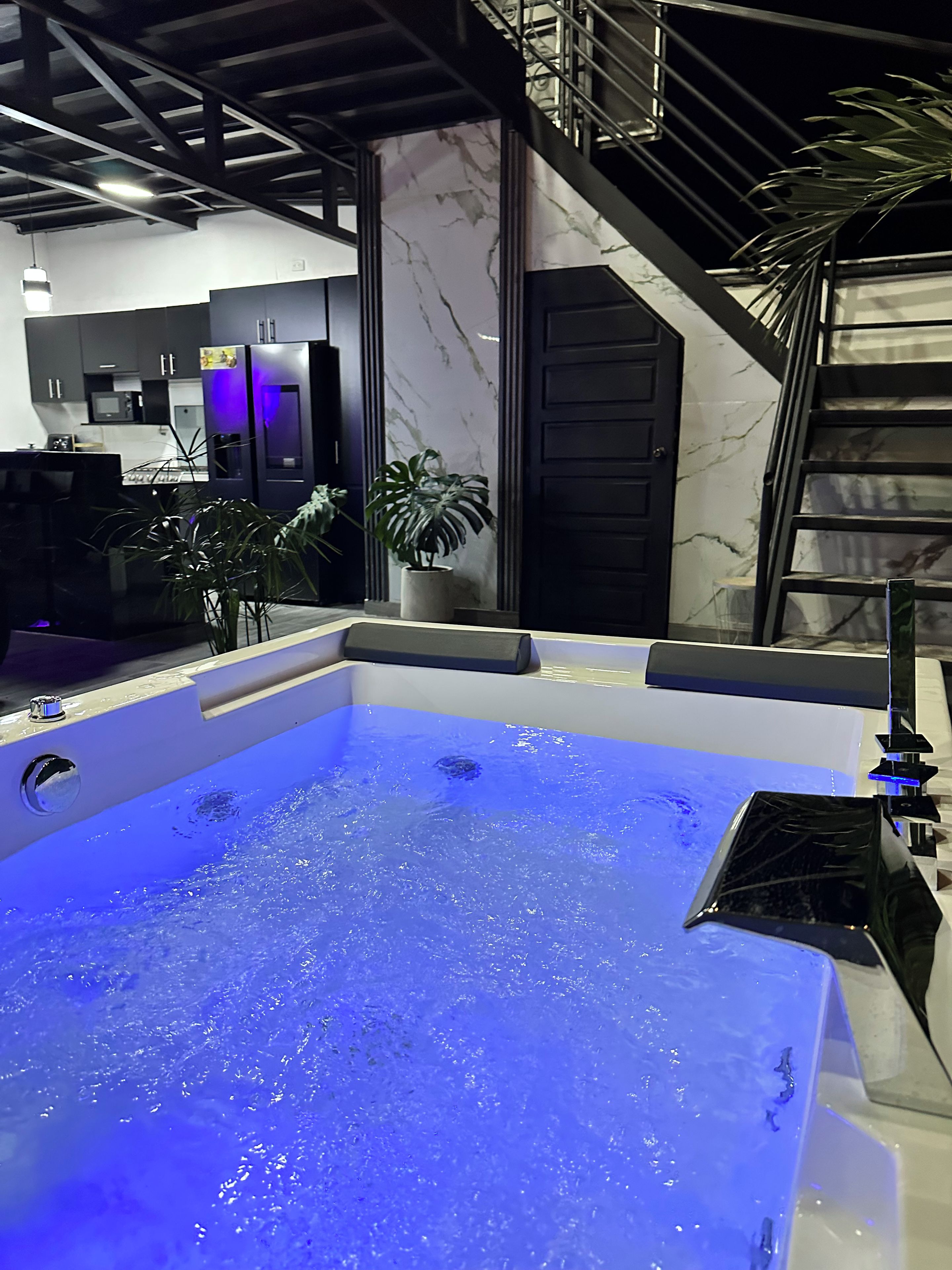 A modern bathroom with a large bathtub, a staircase, and a potted plant.