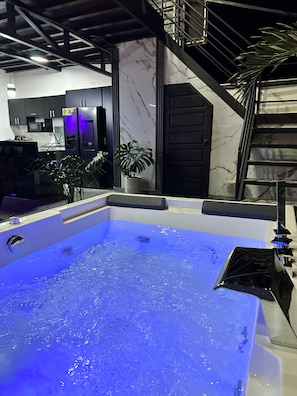 A modern bathroom with a large bathtub, a staircase, and a potted plant.
