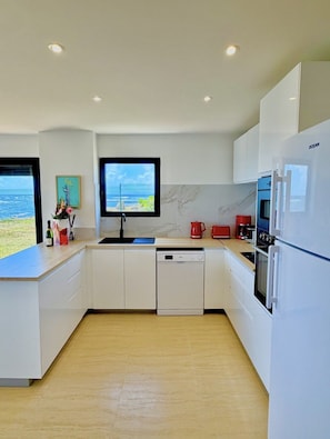A modern kitchen with white cabinetry, a built-in dishwasher, a large refrigerator, and a television mounted on the wall. - SEA VIEW MULLET BAY Villa – Brand-new waterfront villa in Oyster Pond (Oyster Pond)