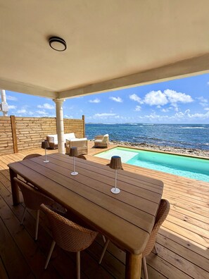An outdoor deck with a wooden table and wicker chairs, overlooking a pool and the ocean. - SEA VIEW MULLET BAY Villa – Brand-new waterfront villa in Oyster Pond (Oyster Pond)