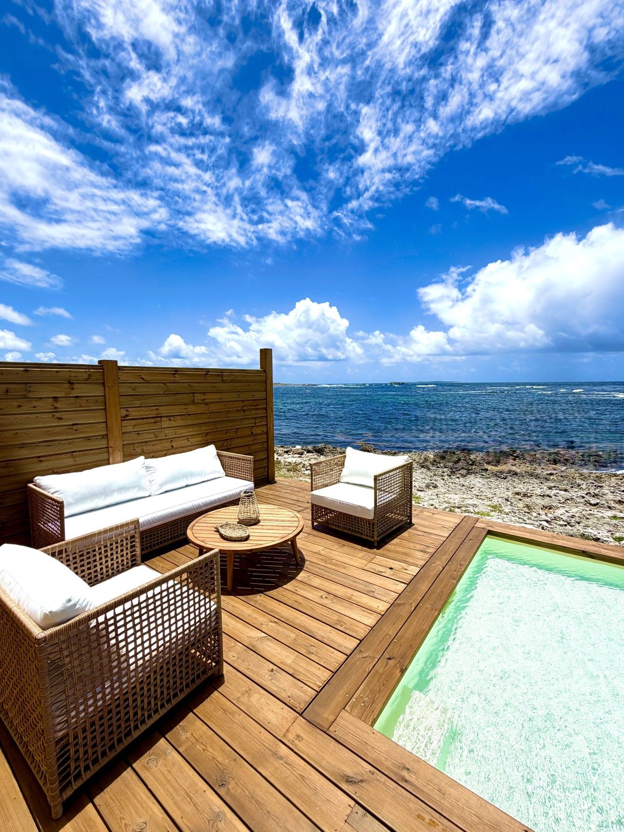 A wooden deck with wicker furniture, a round table, and a small pool.