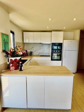 Una cocina moderna con armarios blancos, encimera de madera, horno integrado y refrigerador.