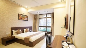 Quarto de hotel com uma cama grande, uma escrivaninha com cadeira, janela com cortinas e um quadro na parede.