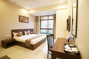 A hotel room with a large bed, a desk with a chair, a window with curtains, and a painting on the wall. - OYO Rooms Trident Road (Udaipur)