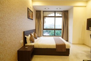 A hotel room with a large bed, a nightstand, a television, and a window with curtains. - OYO Rooms Trident Road (Udaipur)