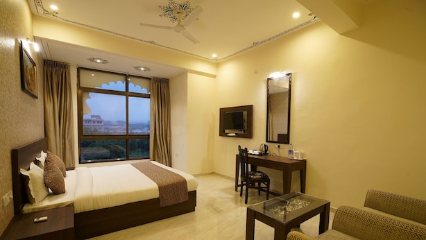 Quarto de hotel com cama, escrivaninha, cadeira, televisão e vista para um edifício pela janela.