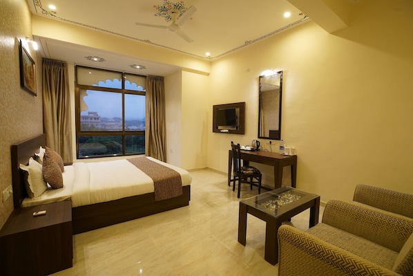 A hotel room with a bed, a desk, a chair, a television, and a view of a building through the window. - OYO Rooms Trident Road (Udaipur)
