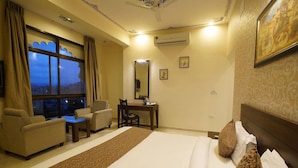 Quarto de hotel com cama, escrivaninha, cadeira, sofá e uma janela grande.