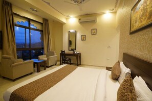 A hotel room with a bed, a desk, a chair, a sofa, and a large window. - OYO Rooms Trident Road (Udaipur)