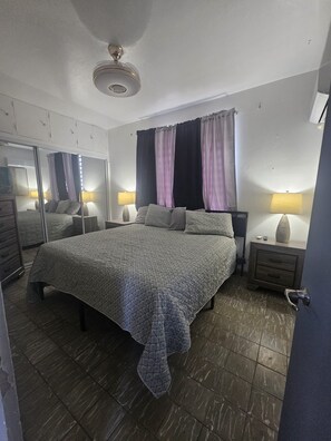 A bedroom with a bed, two bedside tables, a mirror, a window with curtains, and a ceiling fan. - Cozy 1-bedroom apartment in beautiful San Juan with AC (San Juan)