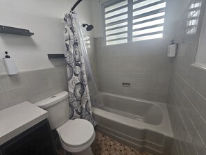 A bathroom with a toilet, bathtub, and shower curtain. - Cozy 1-bedroom apartment in beautiful San Juan with AC (San Juan)