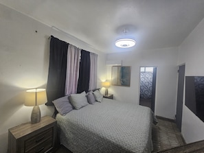 A bedroom with a bed, two bedside lamps, a nightstand, a window with curtains, and a ceiling light fixture. - Cozy 1-bedroom apartment in beautiful San Juan with AC (San Juan)