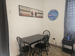 A dining area with a table and chairs, a painting of a beach scene, and a round abstract art piece. - Cozy 1-bedroom apartment in beautiful San Juan with AC (San Juan)
