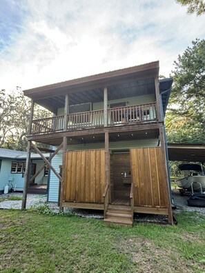 A two-story wooden cabin with a balcony, a porch, and a boat in the background.