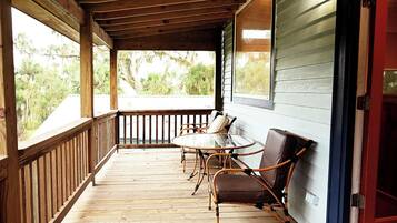A wooden deck with a glass table and chairs, a red door, and a view of greenery.
