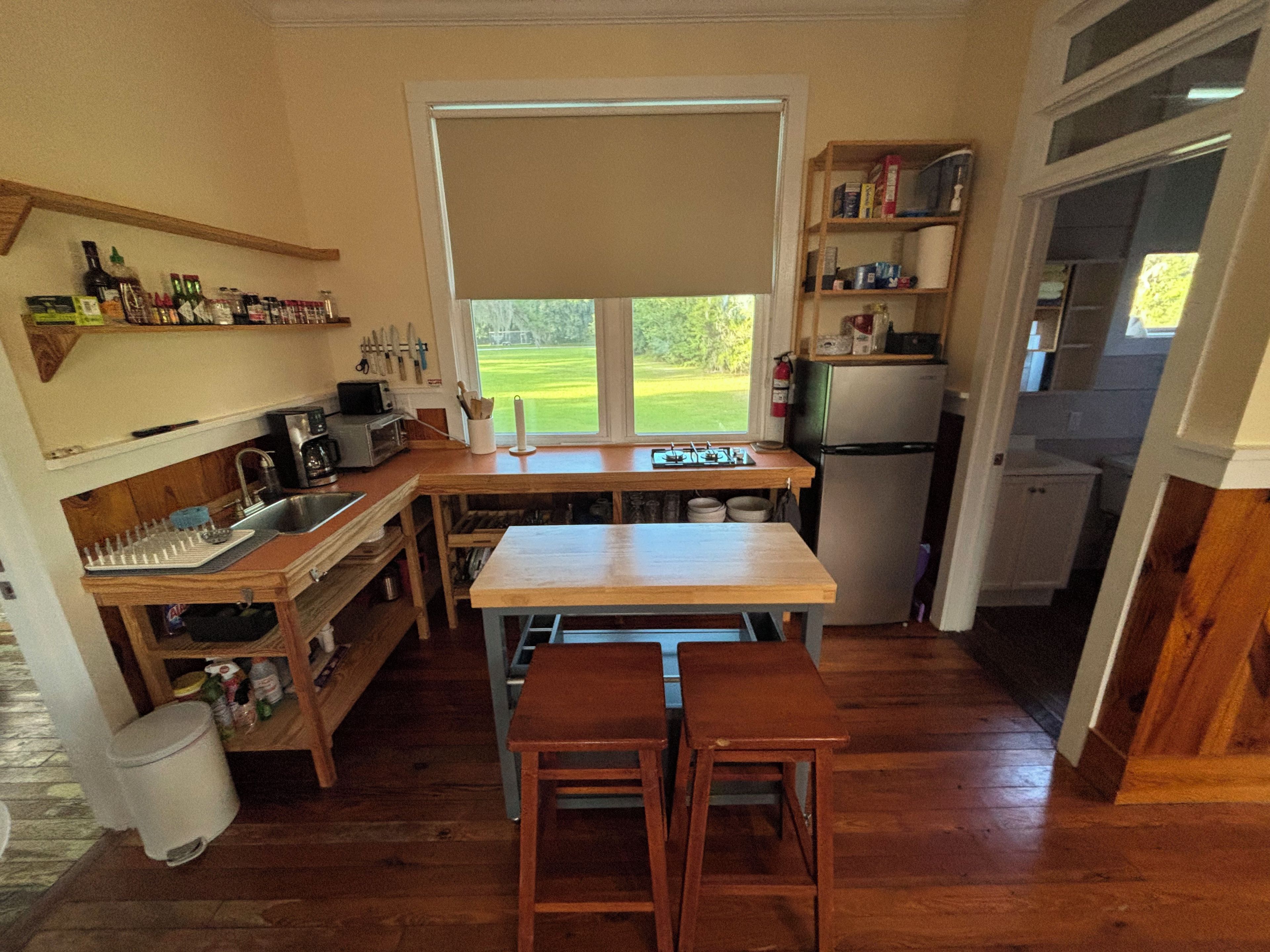 A compact kitchen with a window, wooden cabinets, a sink, and a refrigerator.