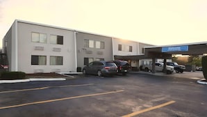 Un hotel con estacionamiento, entrada techada y un cartel que dice 'Bienvenido'.
