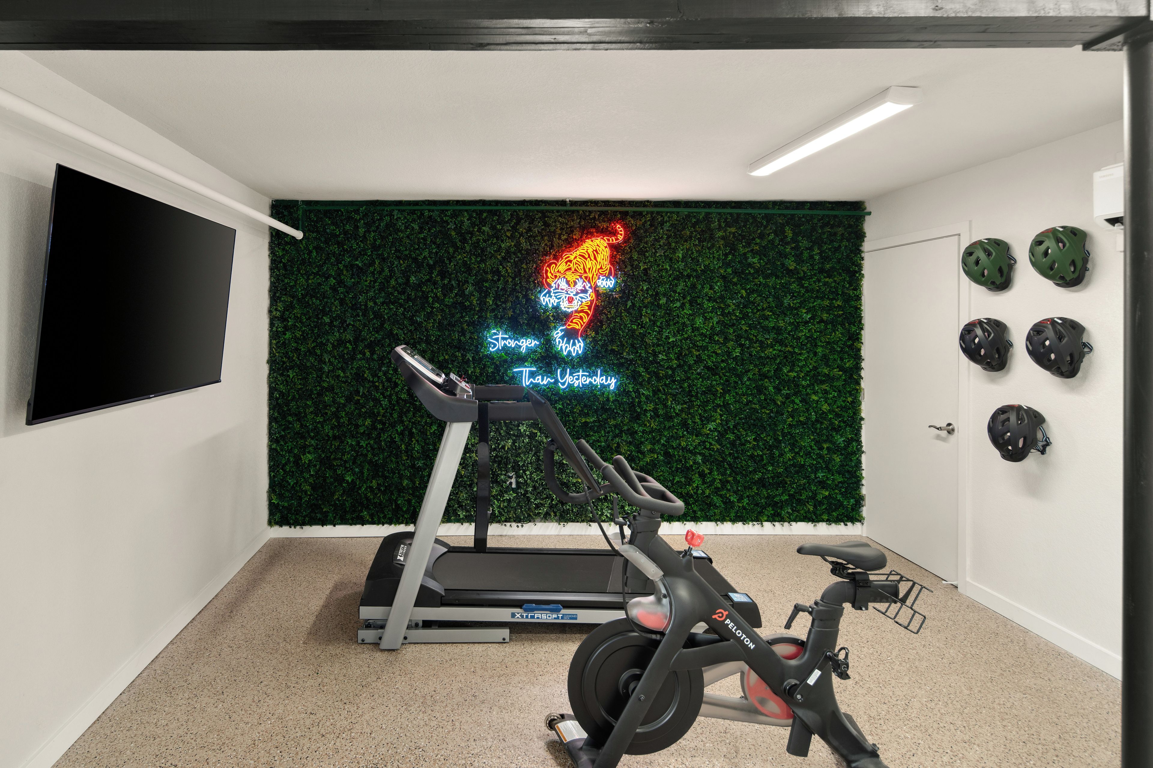 A room with a treadmill, stationary bike, and a neon sign on the wall.