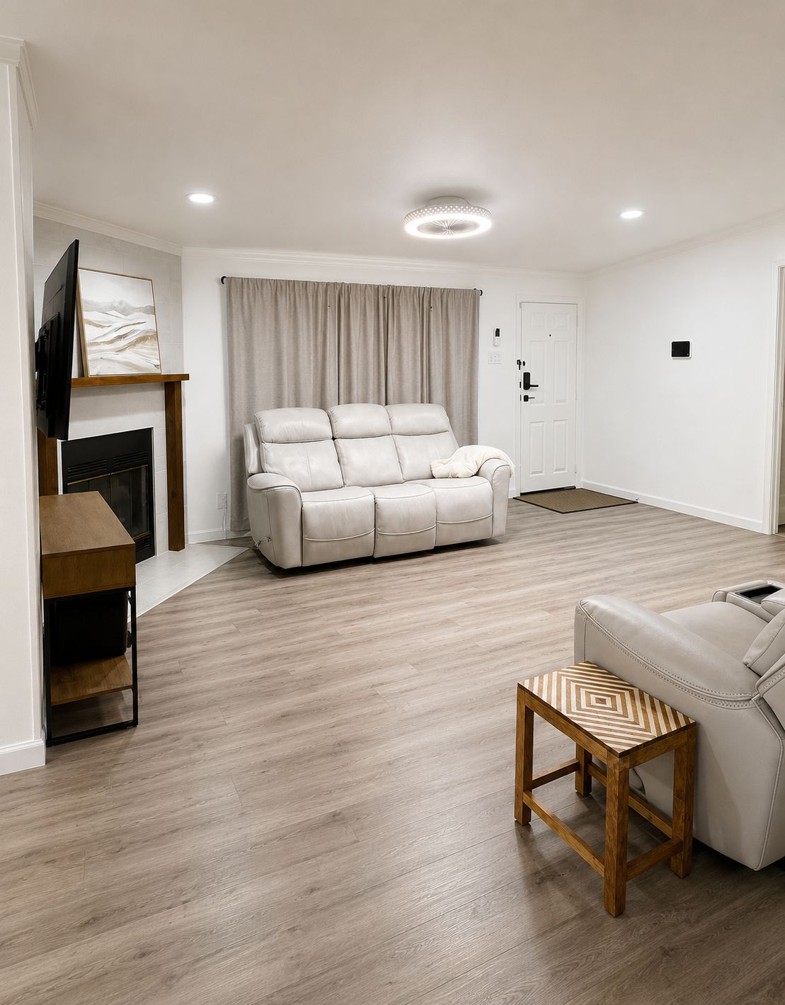 Uma sala de estar moderna com um sofá de couro bege, uma mesa de centro de madeira, uma televisão de tela plana na parede e uma lareira.