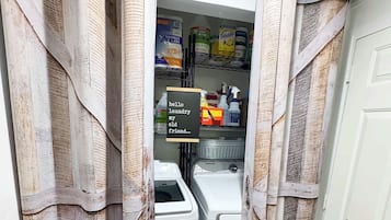 A laundry room with a washing machine, a drying rack, and a shelf with cleaning supplies.