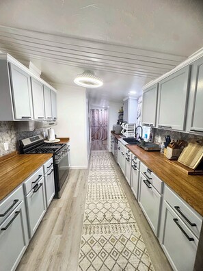 Une cuisine avec des meubles blancs, un plan de travail en bois, un tapis à motifs et un îlot central.