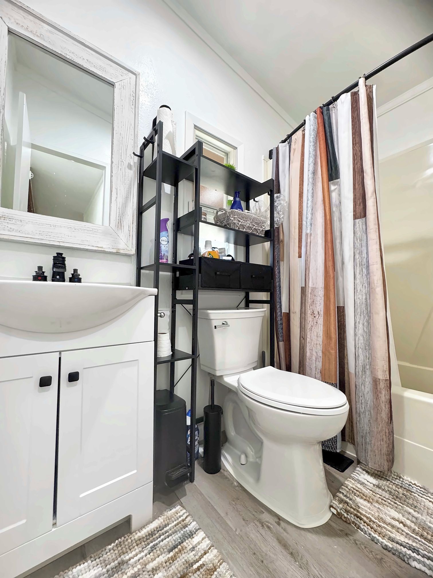 Une salle de bain avec un lavabo blanc, une étagère noire, des toilettes et un rideau de douche.