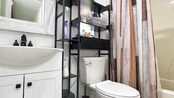Une salle de bain avec un lavabo blanc, une étagère noire, des toilettes et un rideau de douche.