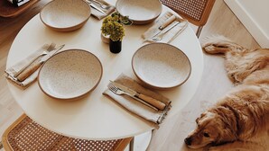 Une table de salle à manger ronde, avec des assiettes à motifs, une petite plante et un golden retriever allongé sur un tapis.