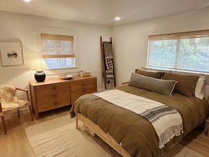 A bedroom with a wooden bed, a nightstand with a lamp, a dresser, and a chair.