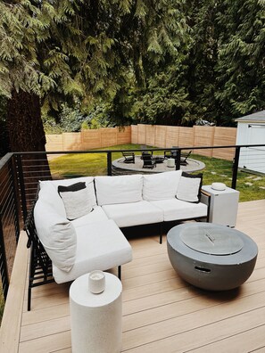 A deck with a white sofa, a round table, and a fire pit.