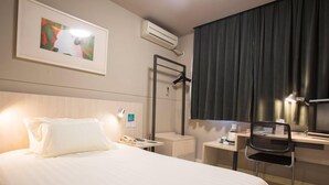 Ett hotellrum med en säng, ett nattduksbord, en stol, ett skrivbord och en tavla på väggen.